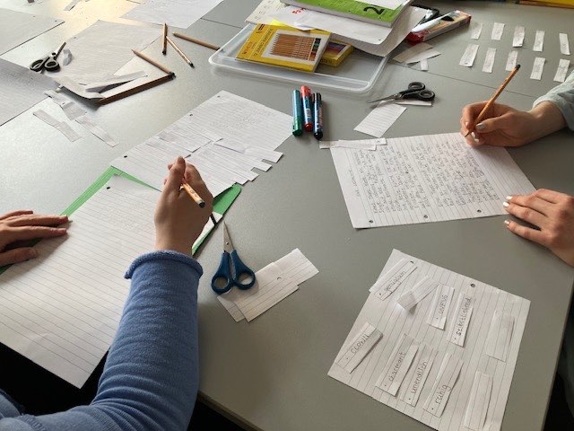 zwei Personen sitzen an einem Tisch mit handgeschriebenen Texten und anderen Zetteln und Textschnipseln